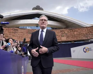 Starmer stands outside near a red carpet with journalists holding microphones to his right
