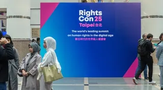 A group of women talking in a large public building before a sign saying RightsCon 25 Taipei