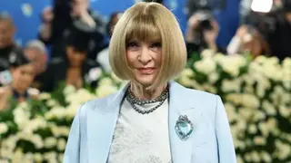Getty Images Anna Wintour, with signature sharp blonde bob and fringe, wears a pale blue outfit with a matching jacket and jewelled brooch - flowers and foliage can be seen behind her