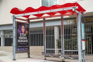 Bus stop shelter with red canopy and ad for Artisan AI reading "Stop Hiring Humans" and "For Work They Hate" on city sidewalk, San Francisco, California, September 30, 2025. (Photo by Smith Collection/Gado/Getty Images)