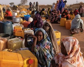 Women and children sit among yellow water containers in an arid refugee settlement