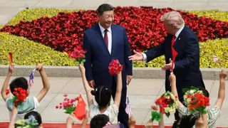 Children wave flags and flowers and lift their arms in the air in front of Xi and Trump, who are standing on a red carpet with Trump gesticulating towards the children
