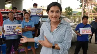 BBC News correspondent Suranjana Tewari wears a striped shirt and stands in front of protesters in the Philippines.