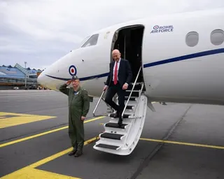 A military service official salutes beside John Healey as he descends from the front of a Dassault Falcon 900LX in Tallinn airport