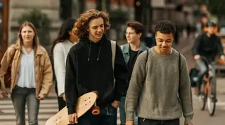 A group of five young people walking in the street one carrying a skateboard