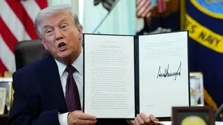 President Donald Trump holding a signed executive order in the Oval Office