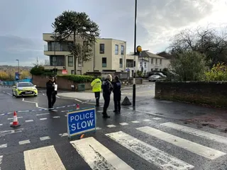 Police officers standing on a street marked off with police tape with a police car in the background