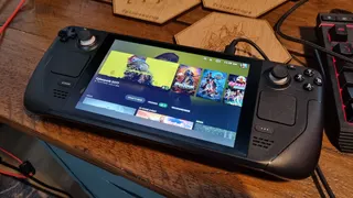 A Steam Deck LCD on a wooden desk, with the SteamOS menu screen on the display