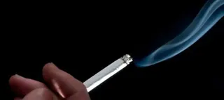 一只手持点燃的香烟，背景为黑色，烟雾袅袅升起。该图像与巴西一项关于烟草消费的公共卫生运动有关。