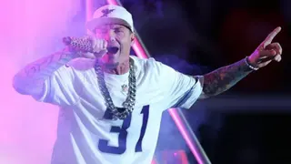Getty Images Vanilla Ice sings into a microphone He wears a white NFL jersey with the number 31 on the front, a white baseball cap and a big silver neck chain.