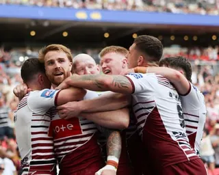 Wigan Warriors players in cherry and white shirts huddle together celebrating after Adam Keighran's try