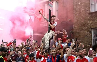 An Arsenal fans holds a red smoke flare as he sits on a lamp-post