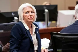 a woman in navy blazer sits in courtroom and looks to side