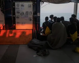 Rescued people wearing life vests sit on the deck of a ship looking out at the sea