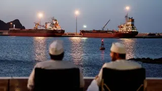 The backs of two men wearing white can be seen looking out to sea, where the Galaxy Globe bulk carrier and the Luojiashan tanker sit anchored as Iran vows to close the Strait of Hormuz, amid the U.S.-Israeli conflict with Iran, in Muscat, Oman, March 9, 2026. REUTERS/Benoit Tessier/File Photo