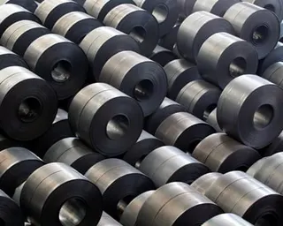 Large coils of rolled steel are stacked together, showing dark and lighter metallic surfaces