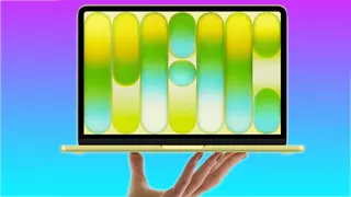 The MacBook Neo in yellow, held aloft.