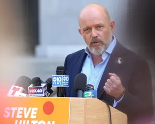 Steve Hilton speaks at a podium with multiple news microphones