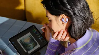 Closeup of a person, wearing the Shokz OpenDots Air earbuds, while sketching on a tablet