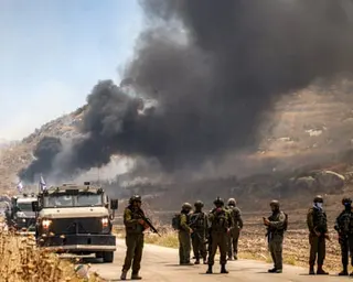 Soldiers stand around on a road with black smoke billowing into the sky behind them