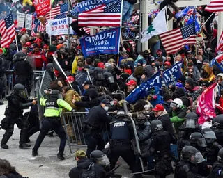 large group holding trump and american flags pushes at barricade while police officers stand on opposite side