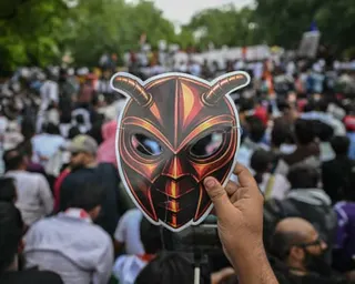 A hand holds up a cockroach mask in front of a large crowd
