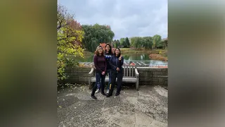 Angelina Resendiz poses with family members in front of a pond surrounded by autumn foliage.