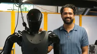 身穿藍色T恤的帕塔克站在黑色的「幻影」機械人旁