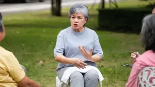 一名頭髮半白的女性坐在兩名接受諮詢的女生對面講解