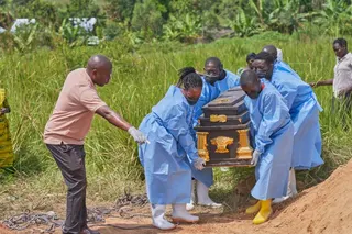 Medical personnel in protective suits carry a coffin.