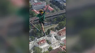 Daredevil Andy Lewis in a green T-shirt and khaki shorts crosses a highline above Bangkok, Thailand