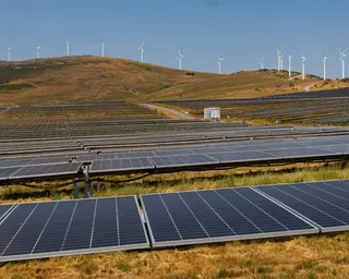 Solar panels in foreground with more panels extending into the distance and wind turbines on hills beyond