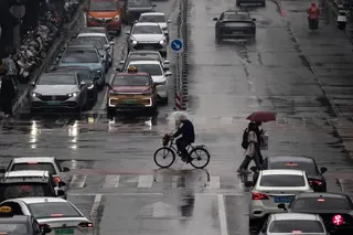 中国今年雨季降水明显偏多，可能冲击粮食生产。图为一名男子在下雨天骑车穿过北京一条马路。 （路透社）