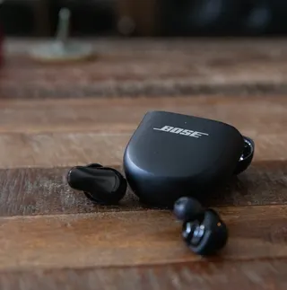 The Bose QuietComfort Ultra Earbuds Gen 2 next to their case on a wooden coffee table.