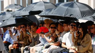 People shield themselves from the sun with umbrellas during Thom Browne’s Spring/Summer 2027 men’s collection show as part of Milan Fashion Week, in Milan, Italy, June 22, 2026.