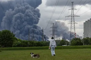 A woman and her dog walk in a park as smoke billows in the background following a reported Ukrainian drone attack in Moscow on June 18. Photo: EPA