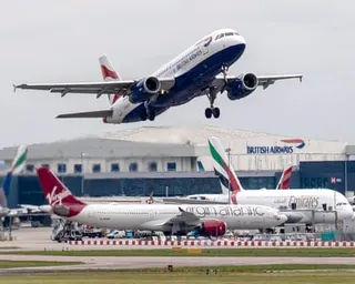 A British Airways plane takes off over grounded aircraft, including a Virgin Atlantic plane at an airport