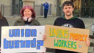 A woman and a man hold signs which read "union busted?" and "unions protect workers"