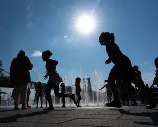 silhouettes of children running by sprinklers outside as sun shines