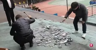 中国湖南郴州菁华园学校教师，在操场上当着学生的面，用铁锤砸烂逾百部没收回来、无人认领的手机，以警示学生不要带手机入校。事件引发中国网民质疑校方粗暴越权实施“铁拳教育”；当地教育局也批评校方处理不当。 （网络视频截图）