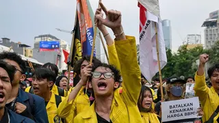 An Indonesian student protester wearing yellow marching on the street in Jakarta with one arm raised