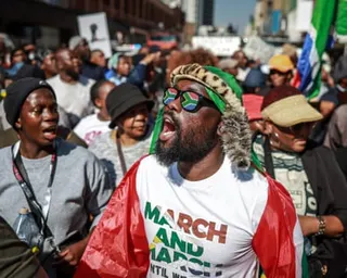 Man wearing South Africa flag sunglasses and a March and March T-shirt shouting in a crowd