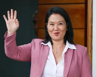 Keiko Fujimori in a pink blazer and white blouse waves while standing in front of a wooden door