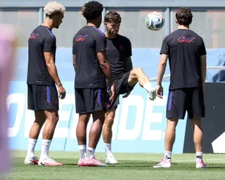 Four soccer players in dark training gear practice with a ball on a grass field