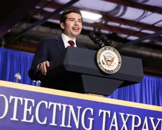 A man speaks at a podium with the vice-presidential seal and a banner reading 'PROTECTING TAXPAY' visible