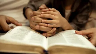 Child's hands praying over a Bible.