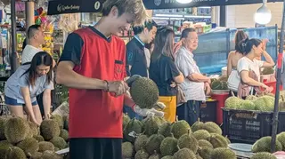 新加坡一位水果攤販正在攤位上開榴槤。