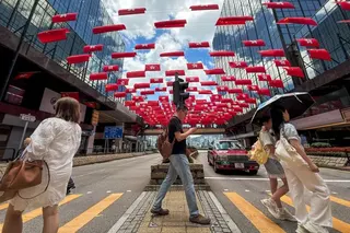 香港街頭，行人走過街道，街道兩旁辦公大樓內懸掛著成排的中國國旗和香港特別行政區旗幟。
