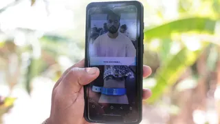 A hand holds a phone displaying the image of a young man in an ICE detention centre