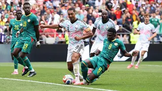 Belgium captain Youri Tielemans is fouled by Lamine Camara during the 2026 World Cup last-32 tie in Seattle. Tielemans is standing with his left leg planted forward as Camara slides in from the side, leading with his right leg. The contact between the pair is difficult to see, with the ball positioned right in front of their pink boots. Behind them, watching on, are two Senegal defenders and two Belgium attackers, including Romelu Lukaku. The Belgians wear white socks and shorts and light shirts
